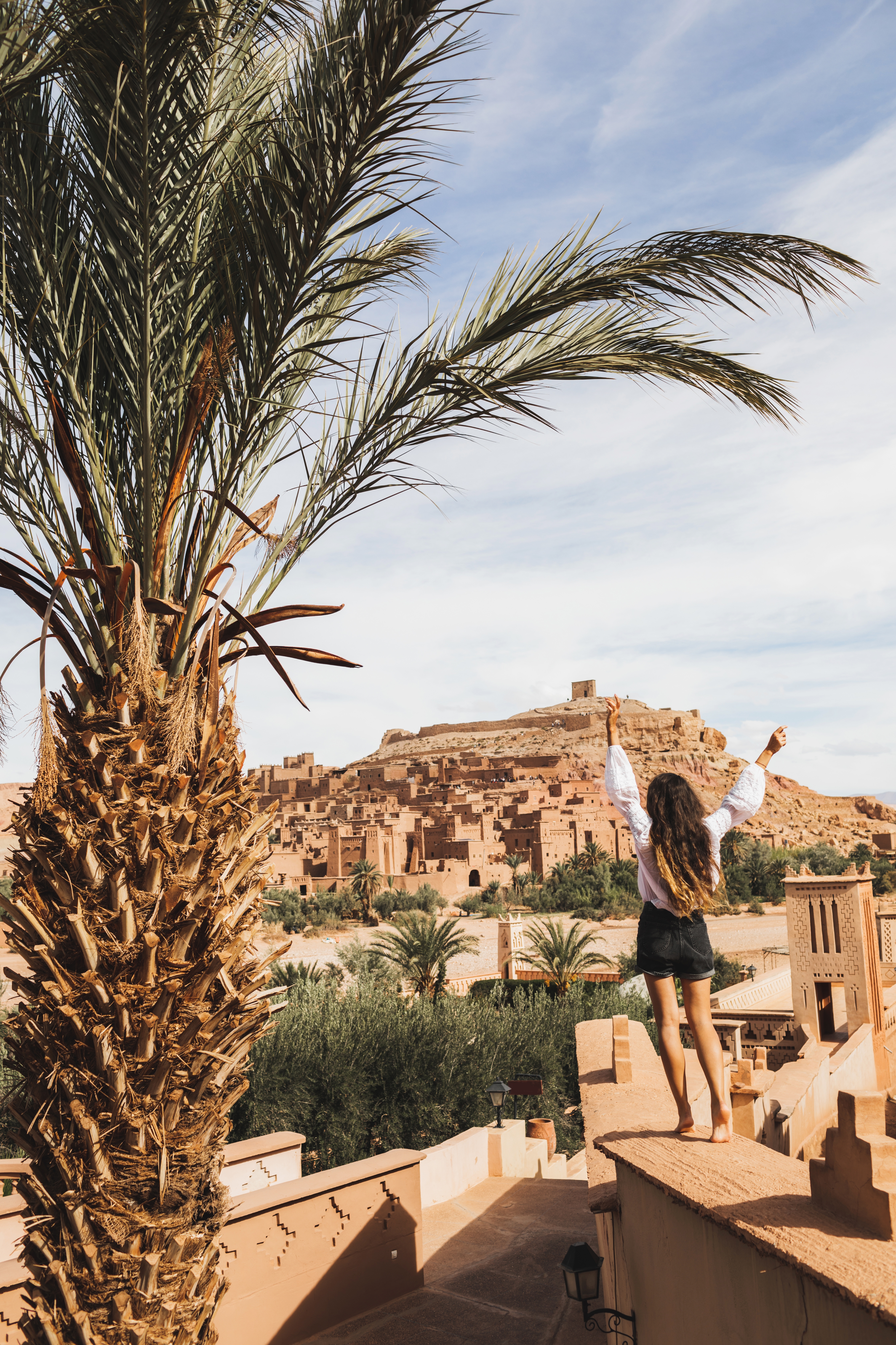Happy woman enjoying famous moroccan landmark ksar Ait-Ben-Haddou. View from behind. Travel Morocco