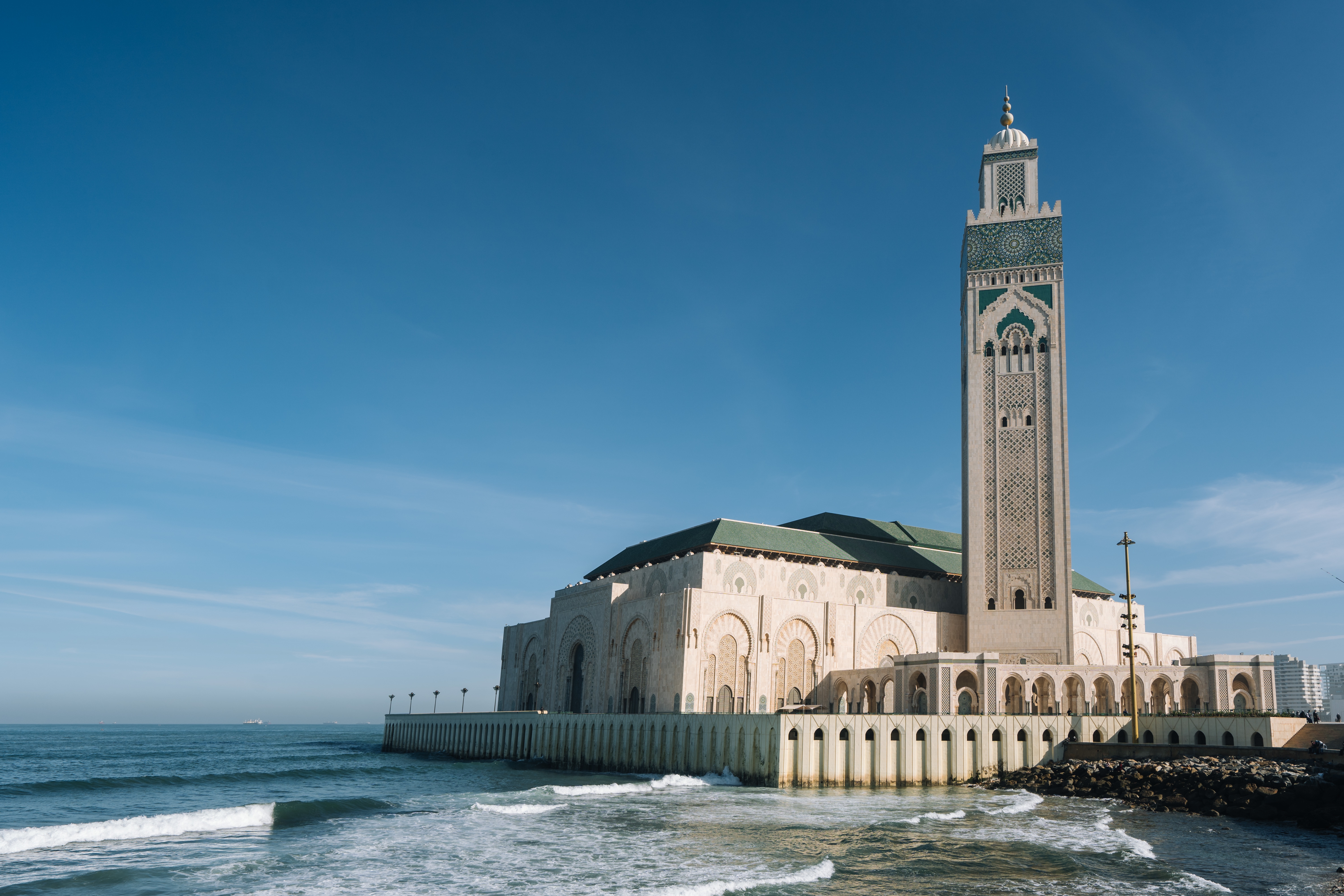 Hassan II Mosque surrounded by water and buildings under a blue sky and sunlight, 6 days tour from marrakech